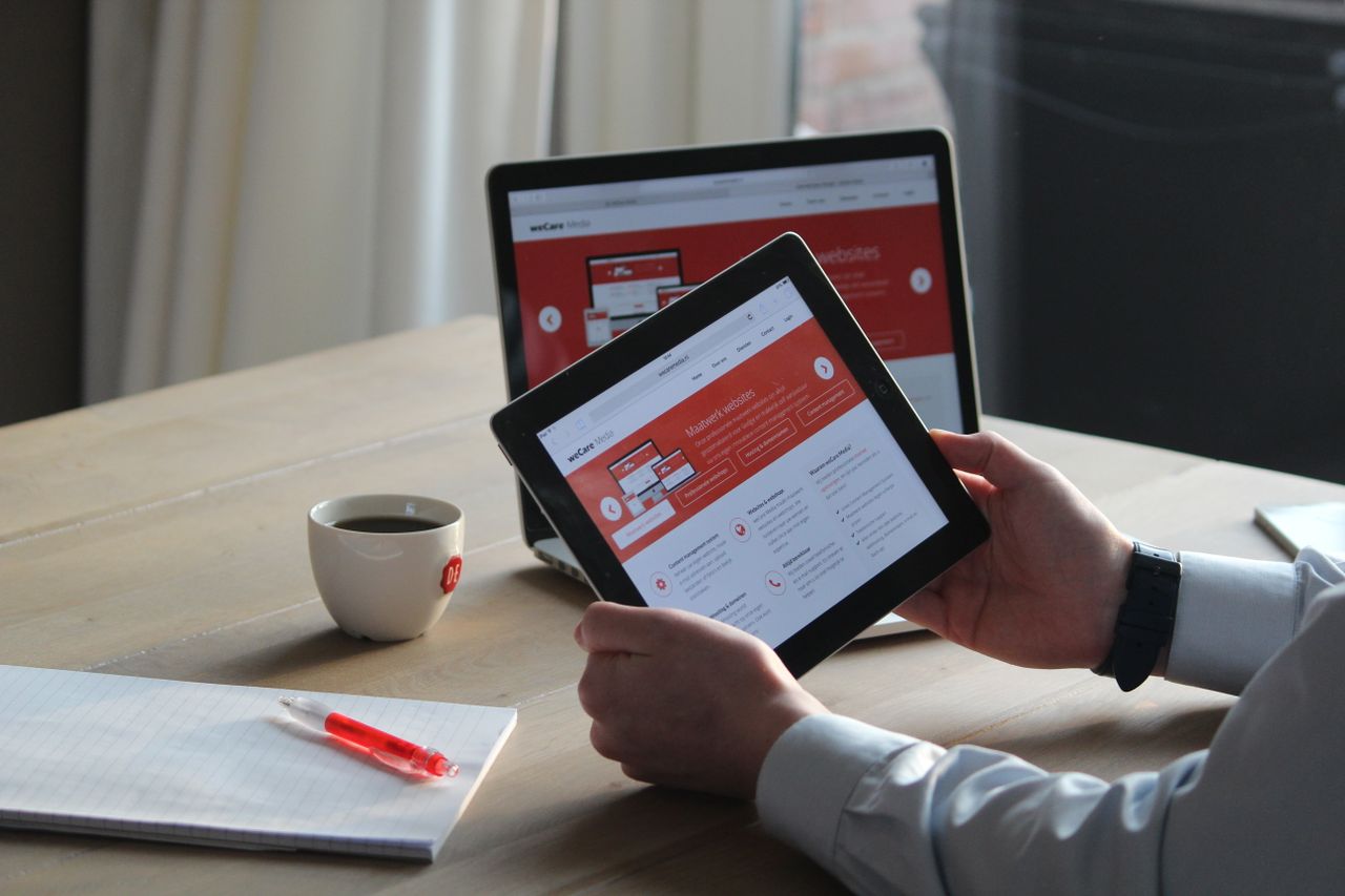 Business professional working with a tablet and laptop beside a hot drink, concentrating on reviewing digital content.